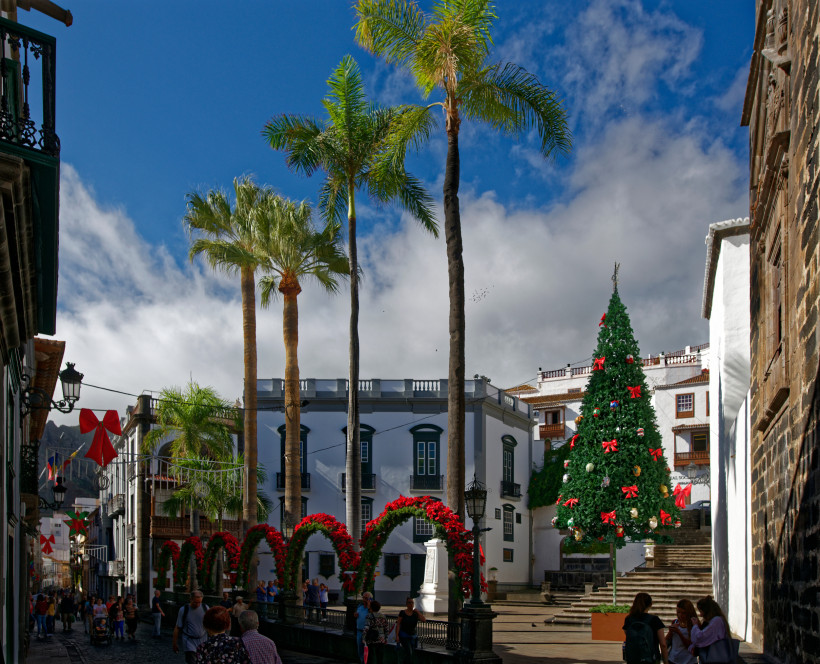 Weihnachten unter Palmen auf den Kanarischen Inseln – festliche Atmosphäre in San Sebastián de La Gomera Weihnachtsbaum mit roten Schleifen auf einem sonnigen Platz mit Palmen und historischen Gebäuden auf den Kanaren