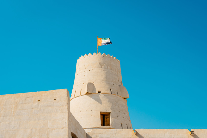 Rundturm des Nationalmuseums Ras Al Khaimah mit Flagge der VAE vor blauem Himmel.