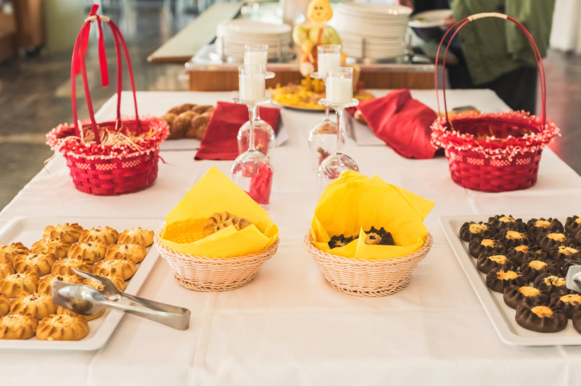 Kreta Ein festlich gedeckter Tisch mit verschiedenen traditionellen Keksen und Plätzchen, darunter helles Gebäck, mit Schokolade überzogene Kekse und zwei kleine Körbe mit gelben Servietten. Im Hintergrund rote Dekokörbchen, Gläser mit Kerzen und Geschirr – all