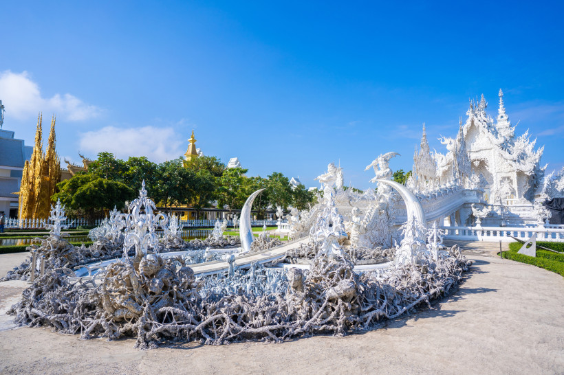 Wat Rong Khun Chiang Rai – Weißer Tempel Sehenswürdigkeit in Thailand Seitliche Ansicht des Weißen Tempels Wat Rong Khun in Chiang Rai, Thailand mit kunstvollen weißen Skulpturen und blauem Himmel.
