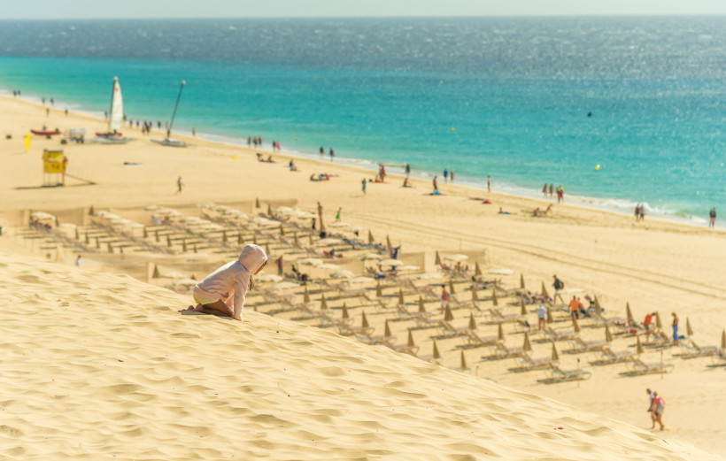 Kind auf einer Sanddüne mit Blick auf den Strand und das Meer in Morro Jable