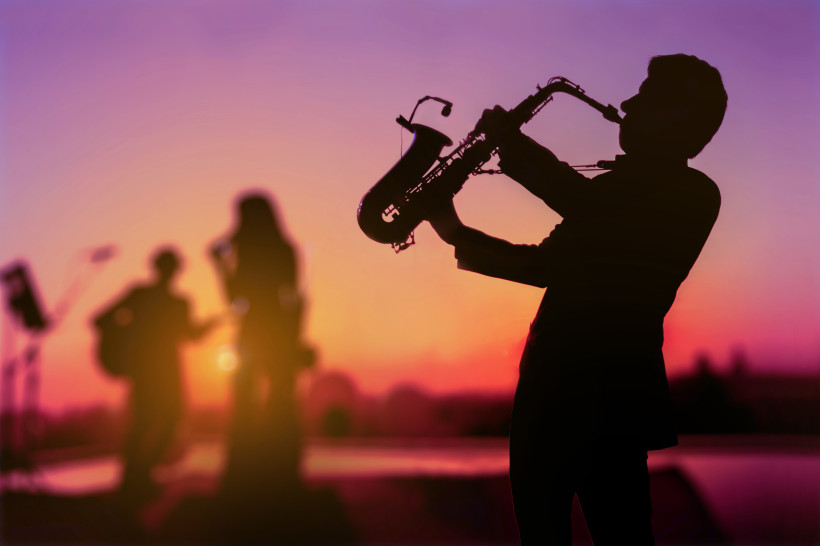 Silhouette eines Saxophonisten in der Dämmerung, der als Triomusiker auftritt. Hintergrund für Festival, verschwommen, Sonnenuntergang