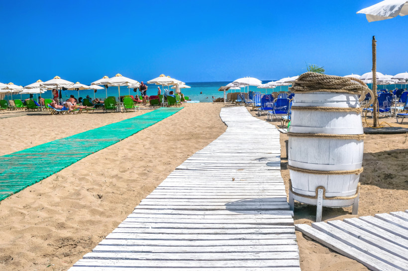 Stalida Strand mit Sand, Sonnenschirmen und Liegen; Holzsteg zum Meer