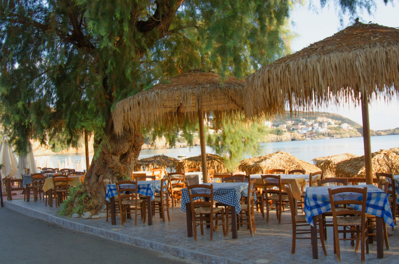 Taverne am Strand von Bali auf Kreta mit Strohschirmen, Tischen und Blick auf die Bucht