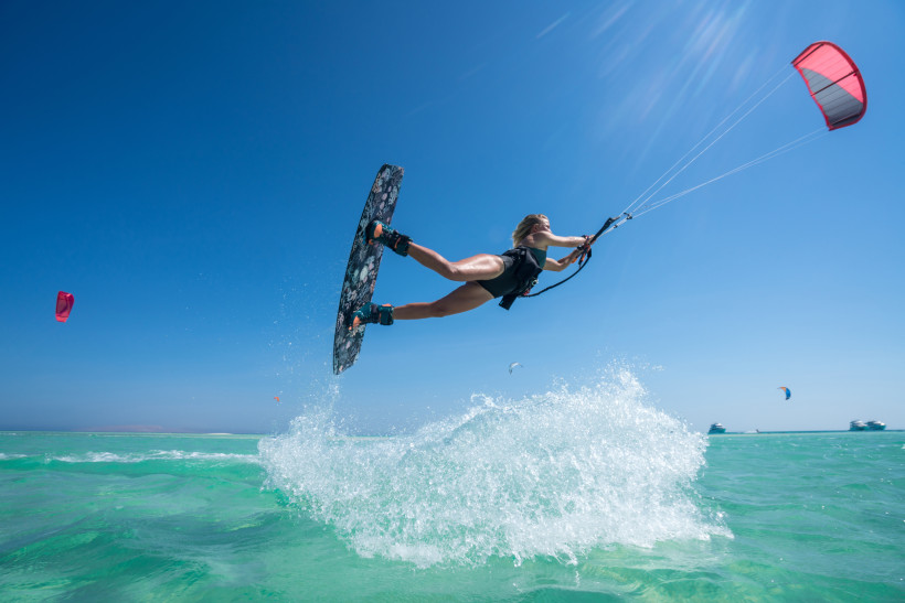 Frau beim Kitesurfen macht einen Sprung über türkisfarbenem Wasser unter strahlend blauem Himmel in der Karibik