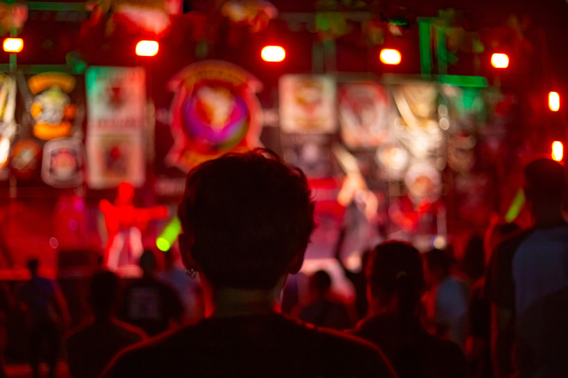 Thailand Pattaya Verschwommene Aufnahme eines Konzert- oder Festivalabends mit bunten Lichtern. Im Vordergrund steht eine Person mit dem Rücken zur Kamera, die auf die hell erleuchtete Bühne mit Live-Musik blickt.
