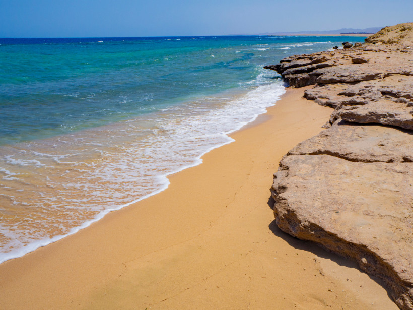 Natürlicher Sandstrand mit türkisblauem Wasser und Felsformationen an der Küste von Marsa Alam in Ägypten.