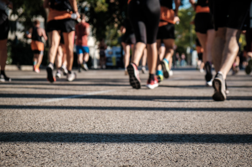 Formentera Nahaufnahme von Beinen und Laufschuhen mehrerer Teilnehmer eines Straßenlaufs. Die Szene zeigt Bewegung und Dynamik auf asphaltierter Straße bei sonnigem Wetter