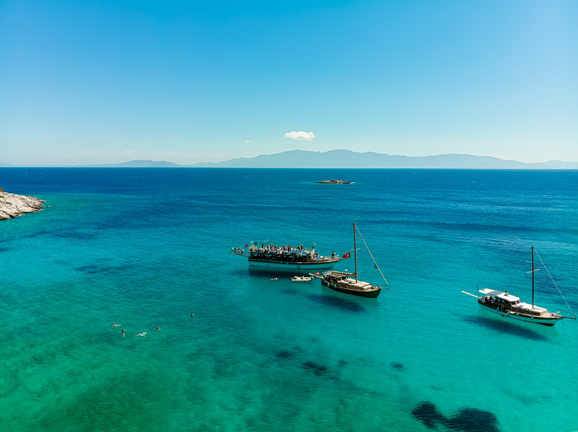 Mehrere Ausflugsboote und Segelboote in ruhiger, türkisfarbener Bucht der Ägäis nahe Bodrum mit Blick auf das offene Meer