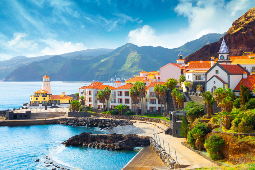 Küstenstadt auf Madeira mit Kirche und Hafen vor grünem Bergpanorama Küstenort auf Madeira mit roten Dächern, Kirche, Hafen und Bergen im Hintergrund