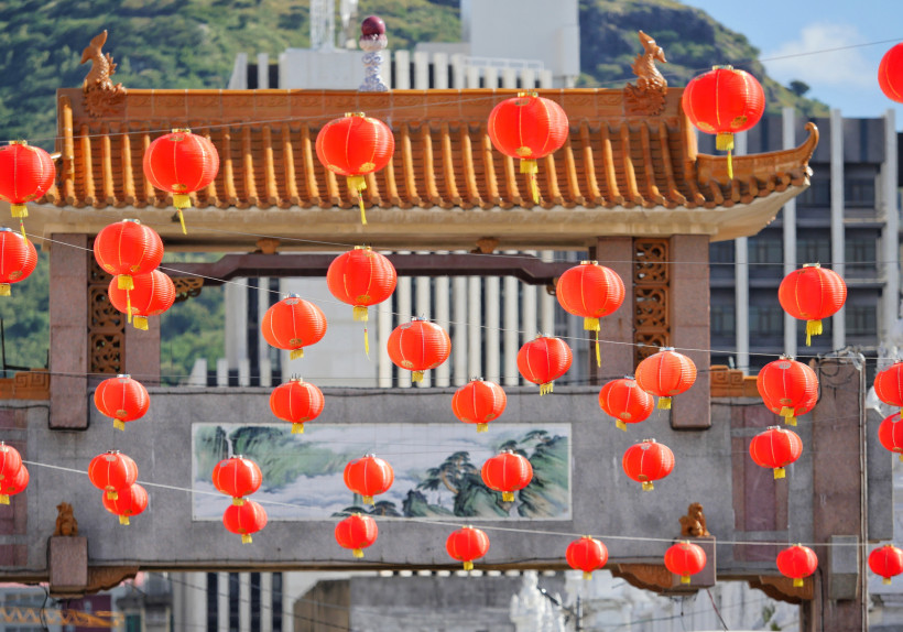 wunderschöne Szene mit einem traditionellen chinesischen Tor, das mit zahlreichen roten Laternen geschmückt ist. Das Tor besitzt ein kunstvoll verziertes, geschwungenes Dach mit Drachenfiguren an den Enden, das an klassische chinesische Architektur erinne