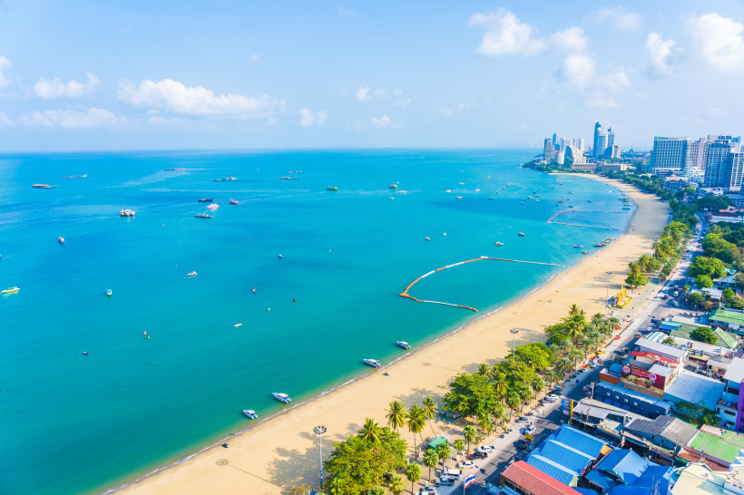 Thailand Pattaya Luftaufnahme von Pattaya Beach mit goldenem Sandstrand, türkisblauem Meer und zahlreichen Booten. Entlang der Küste reihen sich Hochhäuser, Hotels und eine lebhafte Uferstraße.