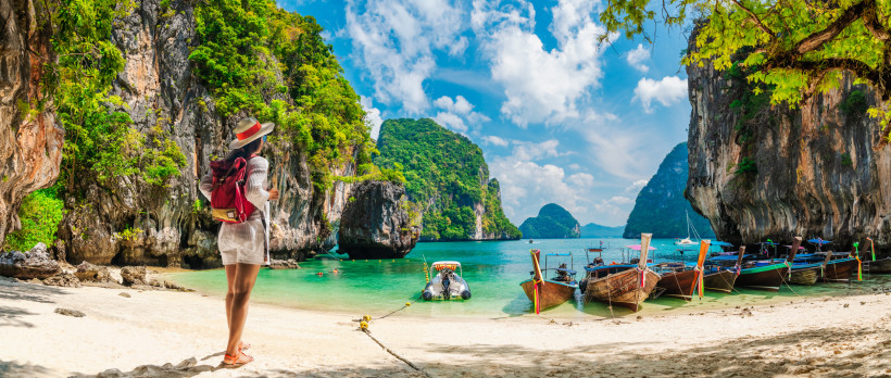 Krabi Strand Thailand – Longtail-Boote, Kalksteinfelsen Touristin steht am Strand von Krabi in Thailand mit Blick auf Longtail-Boote, türkisfarbenes Meer und beeindruckende Kalksteinfelsen.