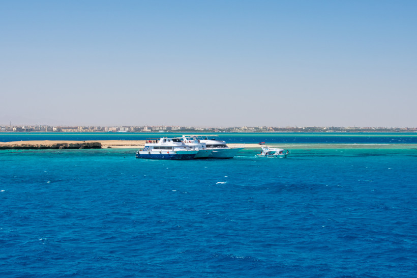 Boote vor der Küste auf dem klaren, blau-türkisen Wasser des Roten Meeres Weiße Ausflugsboote vor einer Sandbank im türkisblauen Roten Meer