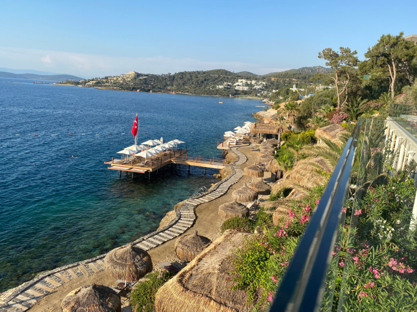 Badeplattform mit Sonnenschirmen und Holzsteg direkt über dem Meer, umgeben von Küste und grüner Landschaft