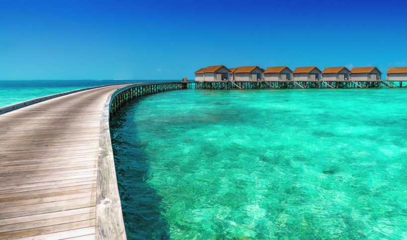 Geschwungener Holzsteg über türkisfarbenem Meer zu Wasserbungalows im Raa Atoll
