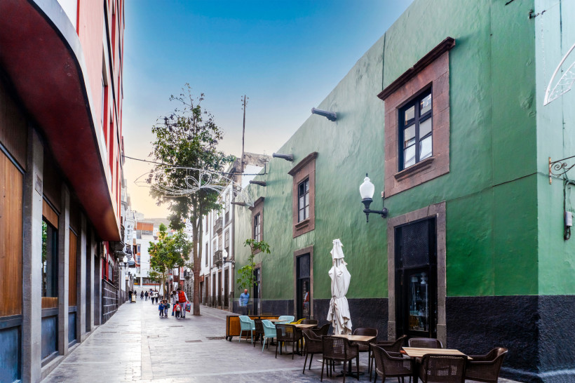 Straßenszene in Triana, Las Palmas, mit grüner Hausfassade, Cafétischen und Stühlen