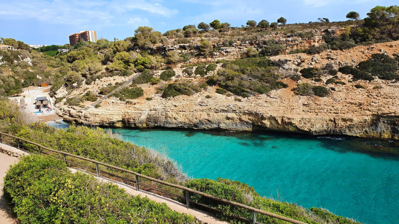 Begehbarer Küstenpfad oberhalb einer Badebucht in Calas de Mallorca mit Blick auf Felsen und klares Wasser