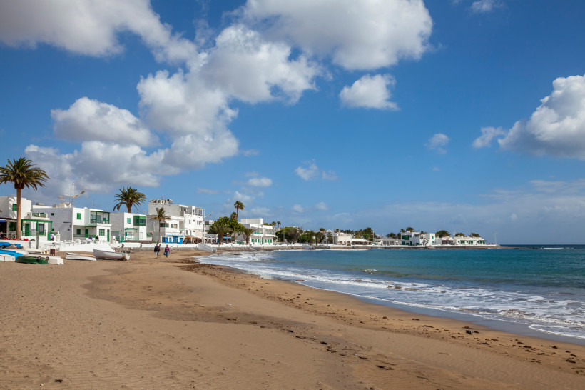 Playa Honda Lanzarote – Ruhiger Sandstrand vor traditionellen weißen Häusern Goldener Sandstrand von Playa Honda auf Lanzarote mit Wellen, Spaziergängern und weißen kanarischen Häusern im Hintergrund.