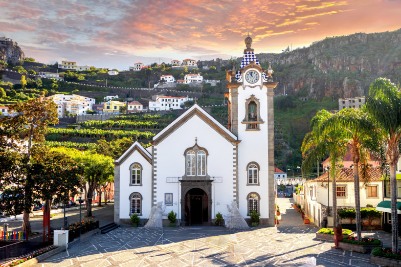 Kirche São Bento in Ribeira Brava auf Madeira mit umliegenden Häusern und Bergen im Sonnenuntergang