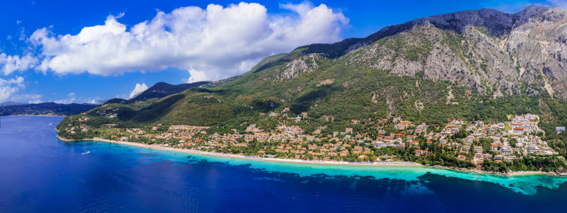 Panoramablick aus der Luft auf Barbati Beach und die Küste vor bewaldeten Bergen Panoramische Luftaufnahme von Barbati Beach mit Küstenort, türkisfarbenem Meer und grünen Berghängen
