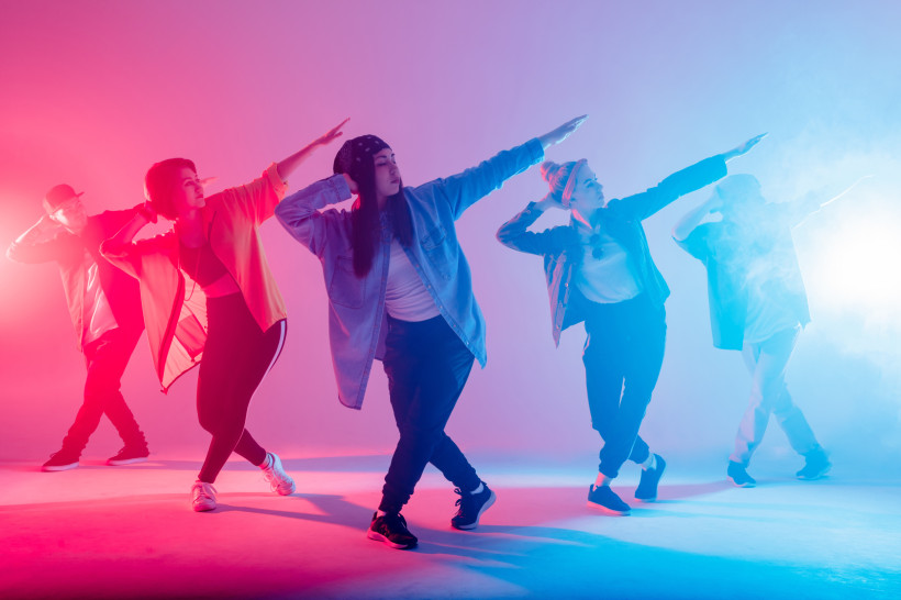 Thailand Pattaya Fünf junge Tänzer:innen in Streetwear posieren synchron unter buntem pink-blauen Bühnenlicht – energiegeladene Hip-Hop-Atmosphäre im Studio