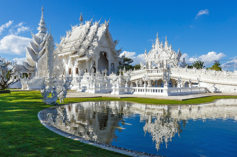 Der Weiße Tempel Wat Rong Khun in Chiang Rai mit reflektierender Spiegelung im Teich und blauer Himmel