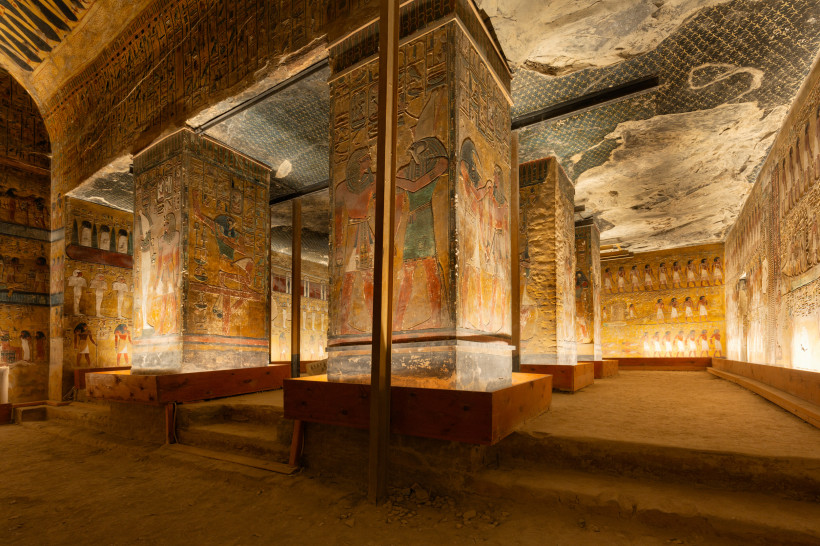 Das Bild zeigt den reich bemalten Innenraum eines altägyptischen Königsgrabes im Tal der Könige. Mehrere große Säulen sind mit farbenfrohen Wandmalereien und Hieroglyphen versehen, die Götter, Pharaonen und rituelle Szenen darstellen. Die Decke ist in dun