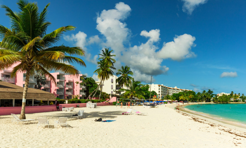 Bunter Palmenstrand mit Hotels und Urlaubern auf Barbados, türkisblaues Meer und blauer Himmel.
