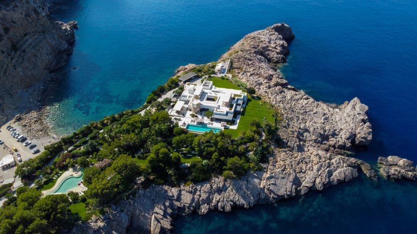 Ibiza Eine luxuriöse weiße Villa mit Pool thront auf einer felsigen Landzunge, umgeben von sattgrüner Landschaft und dem tiefblauen Meer. Die moderne Architektur hebt sich von der Natur ab, während das Anwesen absolute Privatsphäre und traumhafte Ausblicke auf