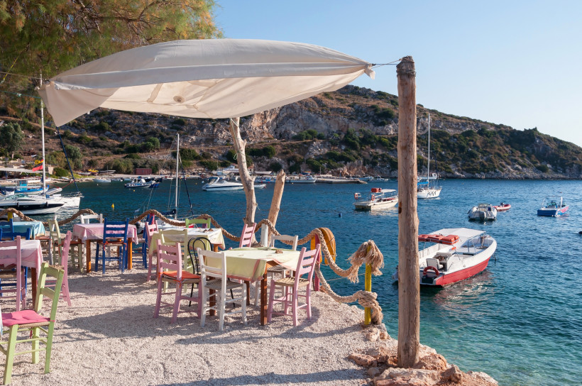 Tische und bunte Stühle in einer Taverne am Wasser, Boote in einer Bucht bei Agios Nikolaos