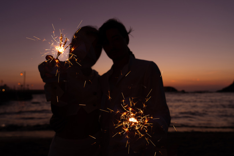 Zwei Menschen am Strand bei Sonnenuntergang halten Wunderkerzen in den Händen, romantische Atmosphäre im Gegenlicht