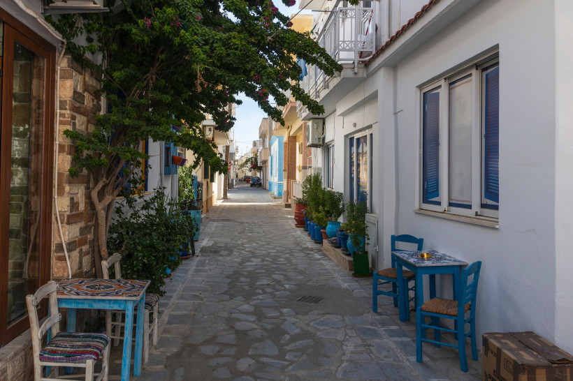 Kos - Kardamena Schmale Gasse auf Kos mit traditionellen weißen Häusern, bunten Fensterläden, Blumen und kleinen Cafétischen mit blauen Stühlen