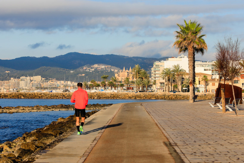Jogger auf der Uferpromenade in Palma de Mallorca mit Meer, Palmen und Bergen im Hintergrund