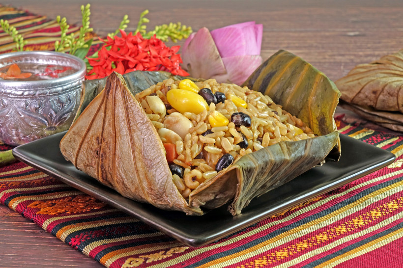 Thailand Pattaya Traditionelles thailändisches Gericht aus gekochtem Reis mit Bohnen, Mais und Nüssen, serviert in einem gefalteten Lotusblatt auf einem schwarzen Teller. Im Hintergrund thailändische Stoffdeko, Blüten und eine verzierte Silberschale.