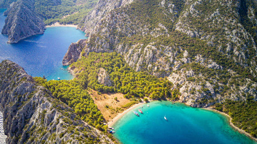 Luftaufnahme mehrerer Buchten bei Kemer mit Booten im türkisblauen Meer und steilen Felsklippen entlang der Küste