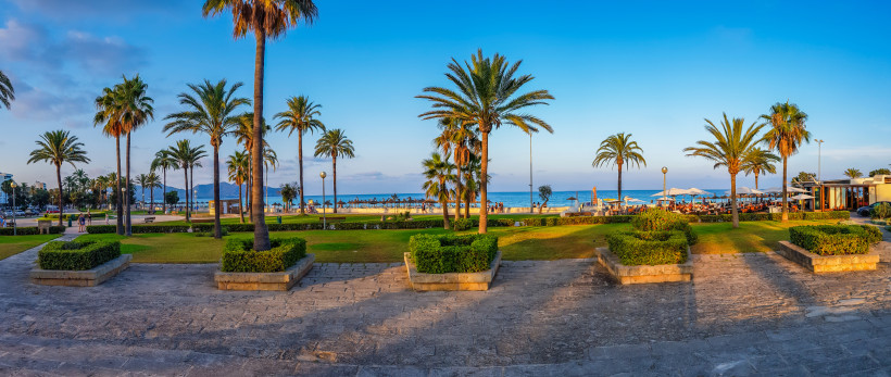 Palmenpromenade in Cala Millor auf Mallorca mit Blick auf das Meer und die Strandbars bei Sonnenuntergang