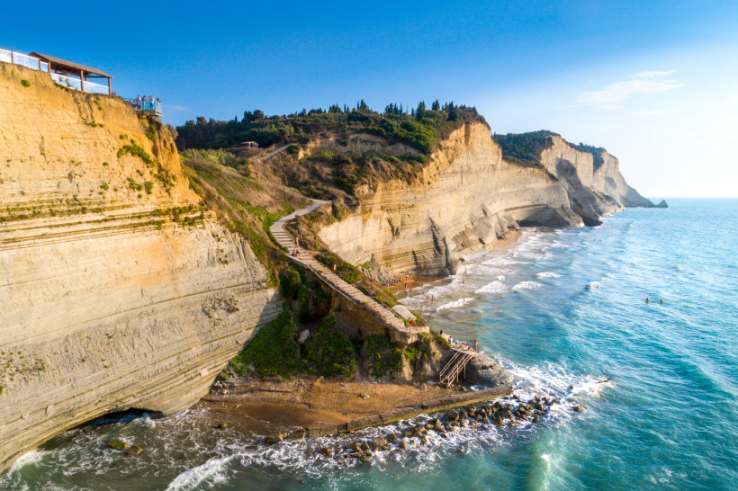 Logas Beach bei Peroulades auf Korfu mit Felsklippen, Treppenweg und Küstenlinie Blick auf die steilen Felsklippen von Logas Beach bei Peroulades auf Korfu mit Treppenweg zum Strand und Meer