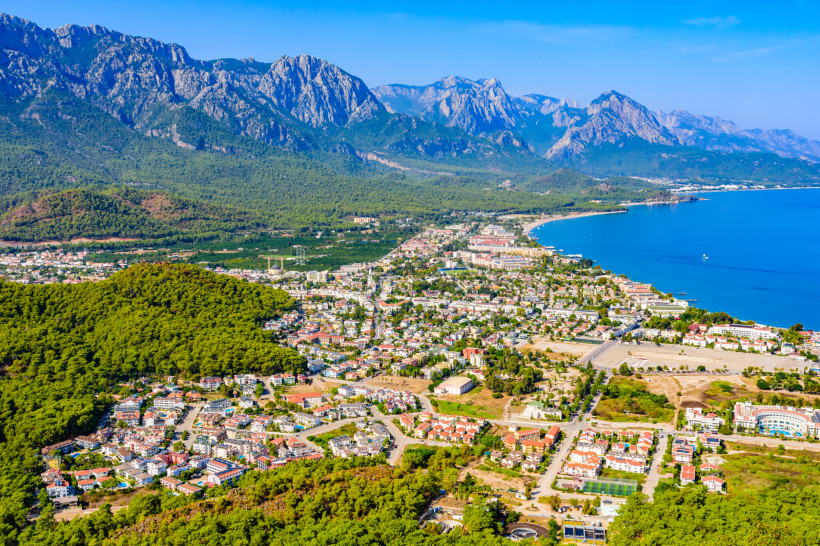 Luftaufnahme von Kemer an der Türkischen Riviera mit Strand, Stadtzentrum, türkisblauem Meer und Taurusgebirge – ideales Reiseziel für einen budgetfreundlichen Urlaub.