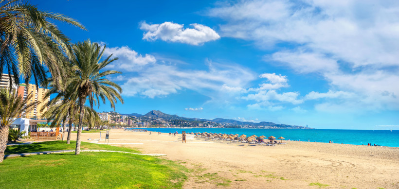 Sandstrand Playa de la Malagueta in Málaga mit Palmen, Sonnenschirmen und Blick auf die Küste und Berge