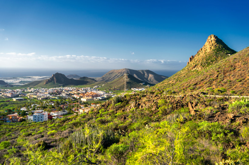 Blick über Valle San Lorenzo auf eine Siedlung und hügelige Vulkanlandschaft unter blauem Himmel