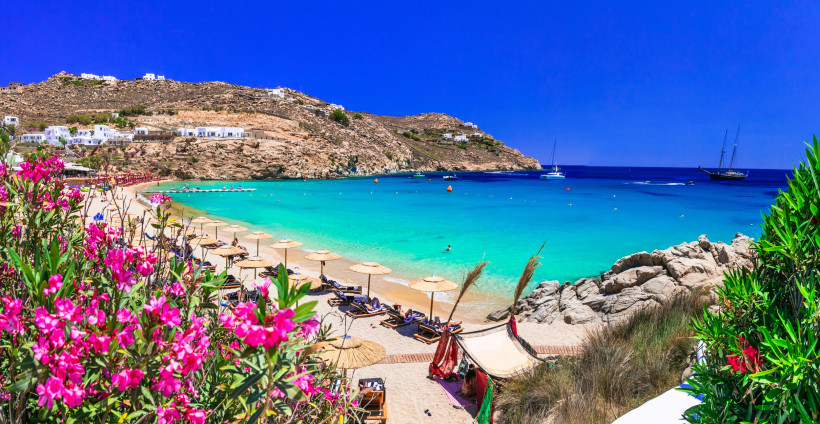 Mykonos - Paradise Beach Blick auf den Beach auf Mykonos mit türkisblauem Meer, Strohdach-Sonnenschirmen und Segelbooten in der Bucht