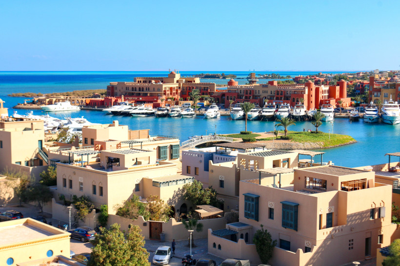 Ägypten - El Gouna Blick auf den Yachthafen von El Gouna, Ägypten. Im Vordergrund befinden sich moderne, helle Wohnhäuser im nubisch-arabischen Stil. Dahinter liegen zahlreiche weiße Luxusyachten vor dem orientalisch anmutenden Gebäudeensemble der Abu Tig Marina. Das tiefbl