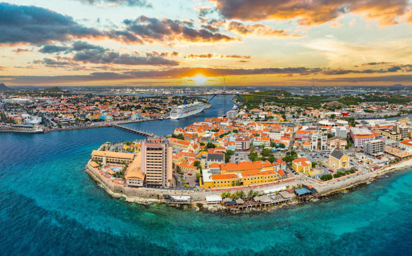 Willemstad – farbenfrohe Altstadt von Curaçao bei Sonnenuntergang Panoramablick auf Willemstad auf Curaçao mit Brücke, Kreuzfahrtschiff und Meer bei Sonnenuntergang