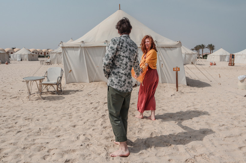Paar spaziert barfuß durch ein Wüstencamp mit großen Zelten in Marsa Alam