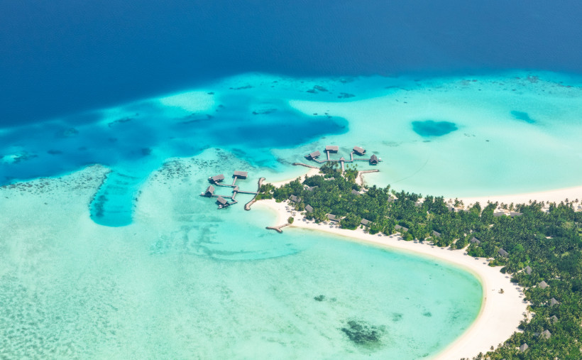 Luftaufnahme einer Insel im Raa Atoll mit Sandstrand, Palmenbewuchs und Bungalows über der Lagune