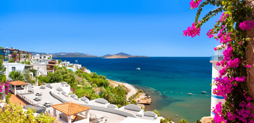 Mediterraner Küstenort an der türkischen Ägäis mit weißen Häusern, türkisblauem Meer, Badebucht und blühender Bougainvillea