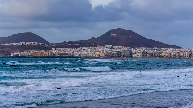 Brandung am Strand La Cícer mit Blick auf die Stadt und die Hügel im Hintergrund