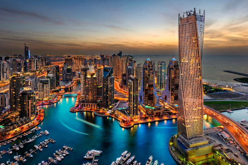 Dubai Marina Bay Beleuchtete Skyline mit verdrehtem Hochhaus und Yachthafen bei Sonnenuntergang, moderne Hochhäuser und Boote vor der Küste einer Großstadt