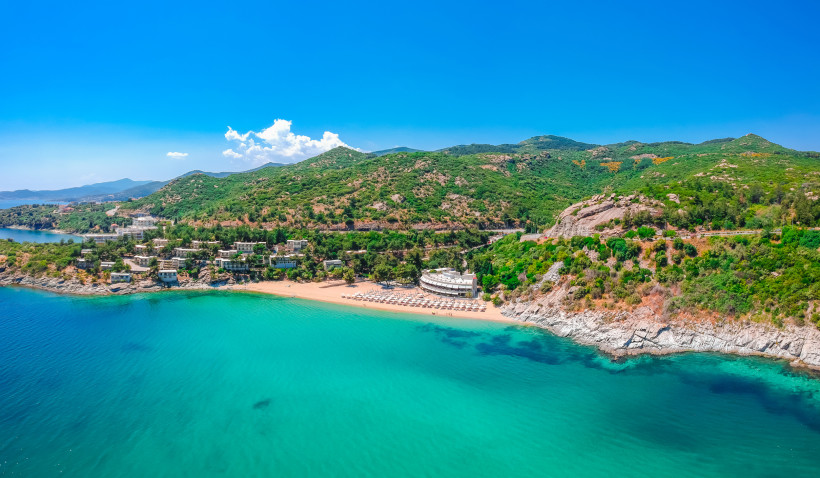 Griechenland - Kavala Batis Beach bei Kavala: halbmondförmige Sandbucht mit türkisblauem Wasser, Liegen und Schirmen, Hotelanlage direkt am Ufer vor grünen Hügeln.